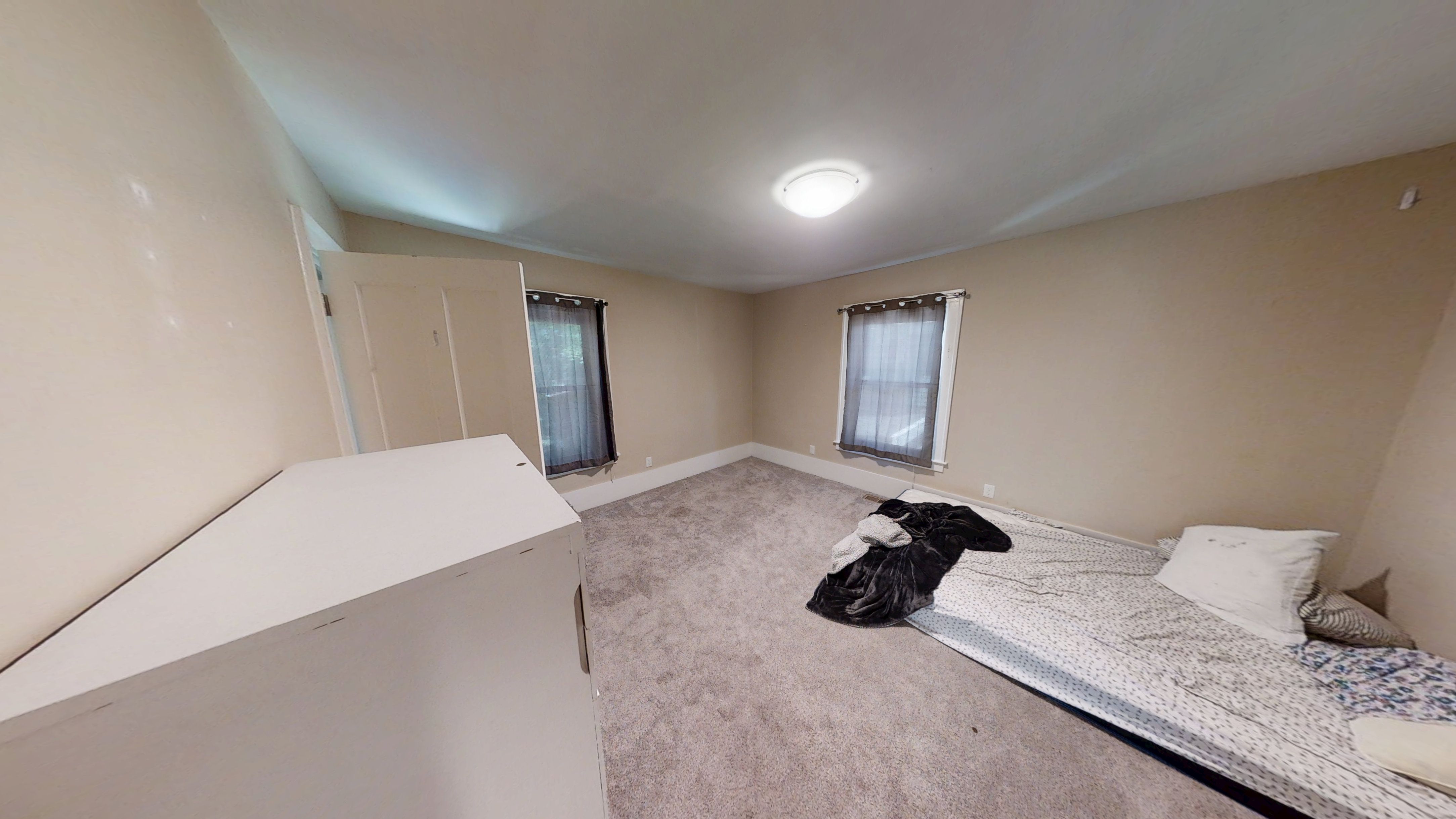 A bedroom with a bed, pillow, and a window with curtains.